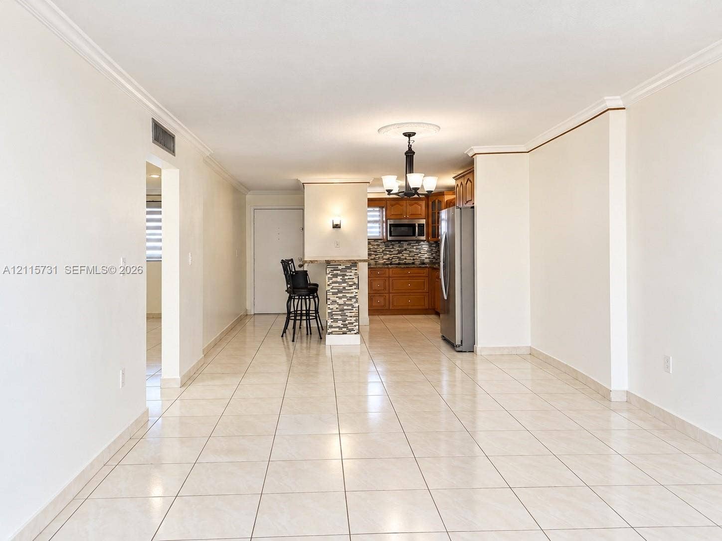 Open-concept interior featuring neutral tile flooring, built-in breakfast bar with stone-finish cladding, wood-finish cabinetry, and crown molding