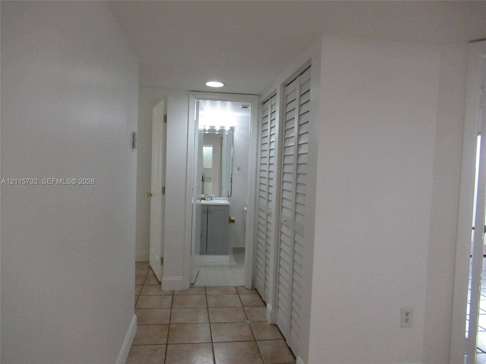 Neutral-toned ceramic floor tile with white louvered-style bi-fold closet doors and recessed ceiling lighting