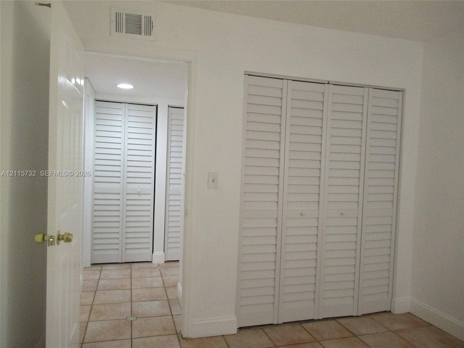 Interior space featuring white louvered bifold closet doors and neutral-toned ceramic tile flooring