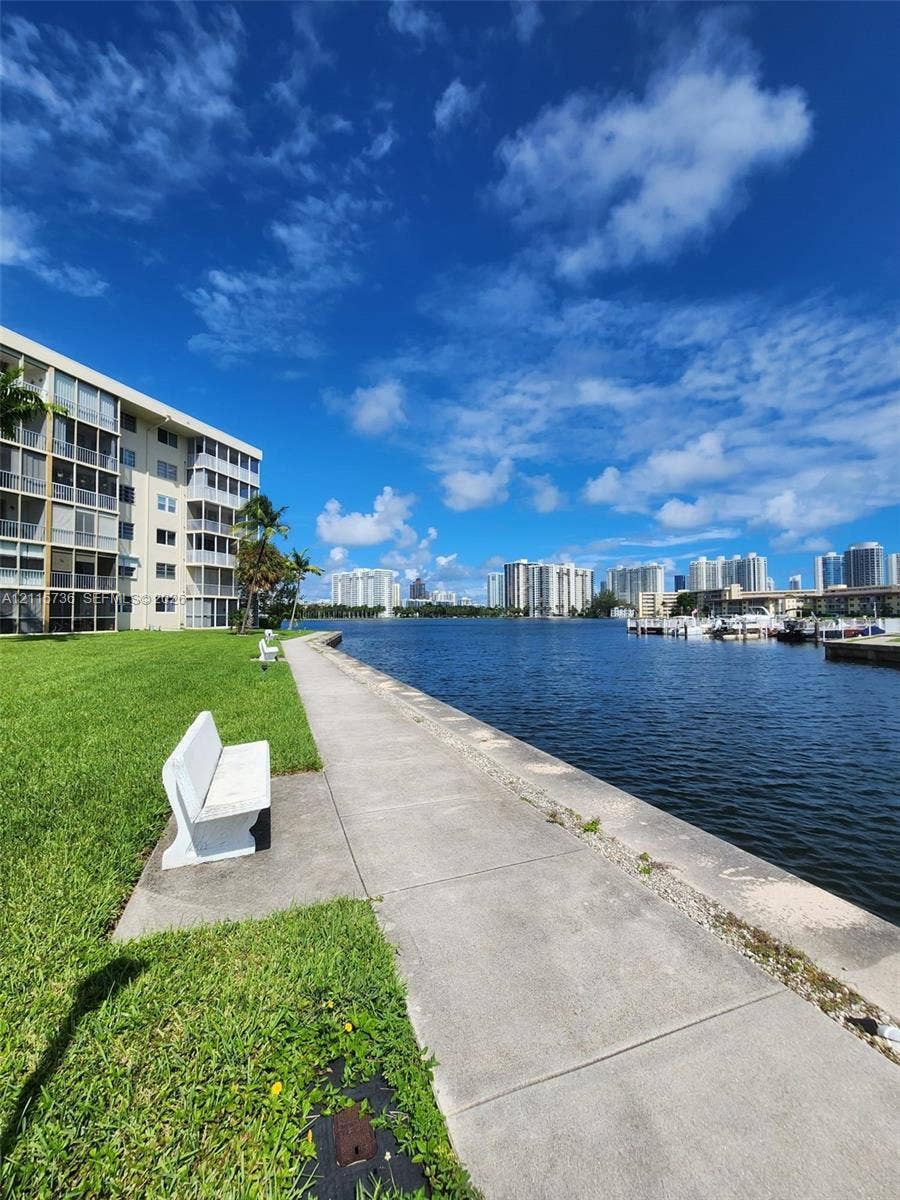 2861 Leonard Drive, #F605, Aventura, FL 33160 Waterfront grounds featuring a concrete bulkhead, paved walkway, manicured lawn, and fixed stone seating