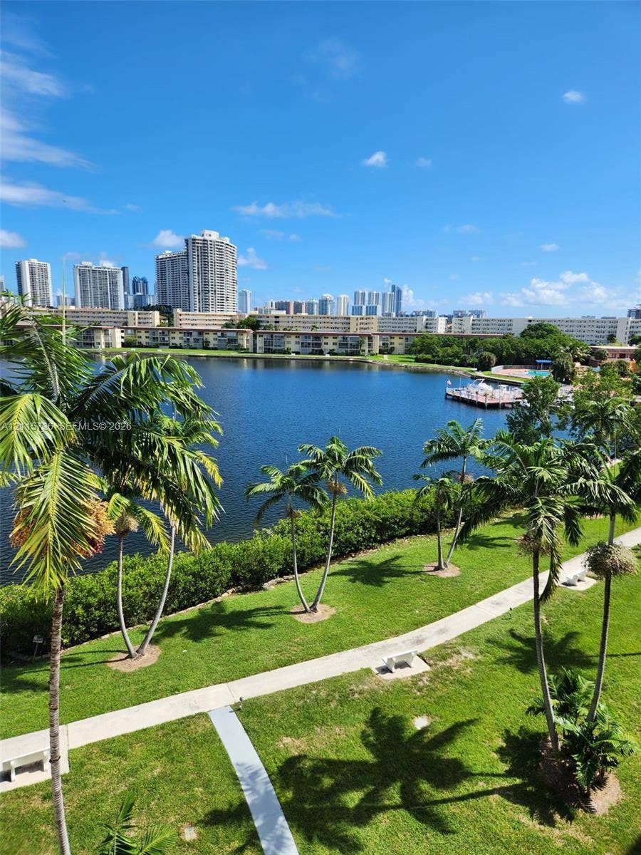 2861 Leonard Drive, #F605, Aventura, FL 33160 Waterfront property grounds featuring a lake, paved walking paths, mature palm trees, and a wooden dock