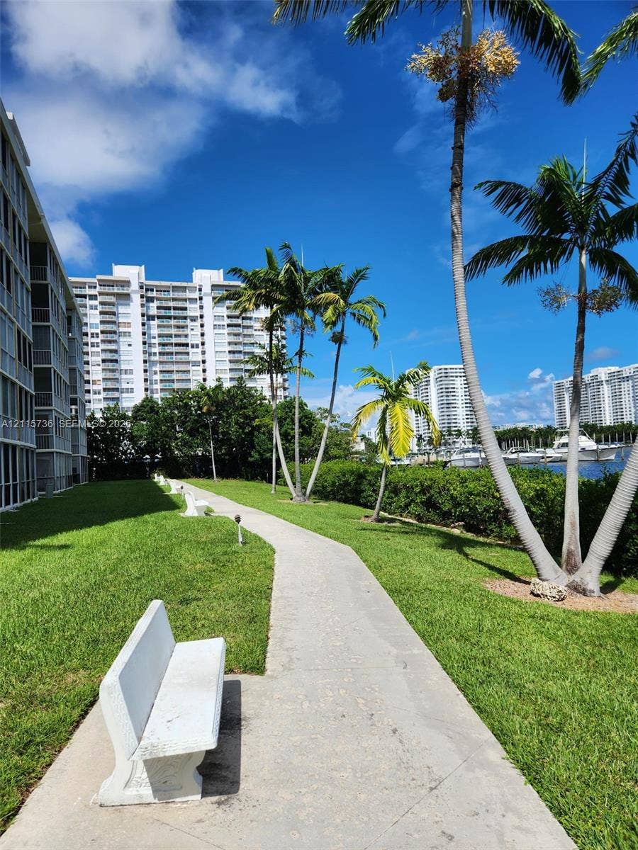 2861 Leonard Drive, #F605, Aventura, FL 33160 Concrete walking path featuring manicured landscaping, mature palm trees, and built-in stone benches