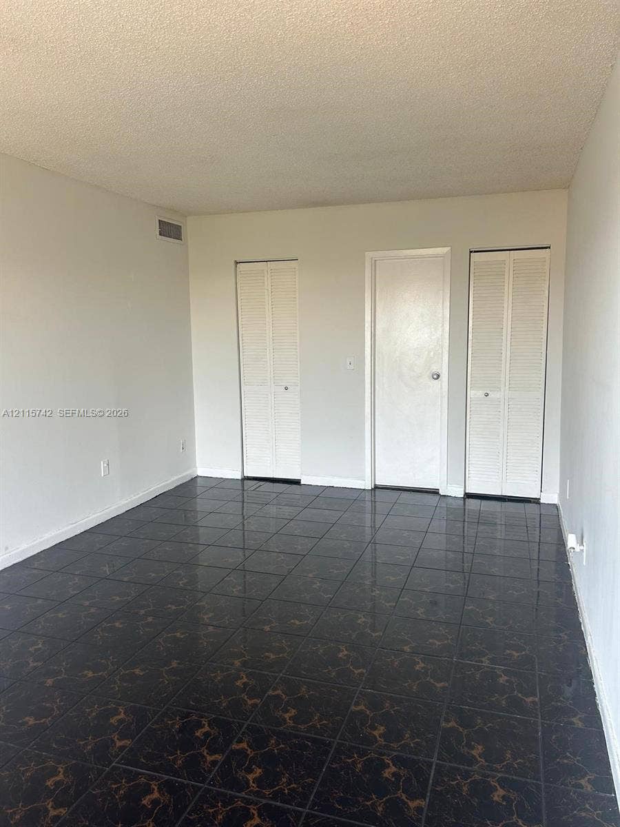 13499 Biscayne Boulevard, #905, North Miami, North Miami, FL 33181 Interior space featuring dark, patterned tile flooring, dual louvered-style closet doors, and a solid-panel door