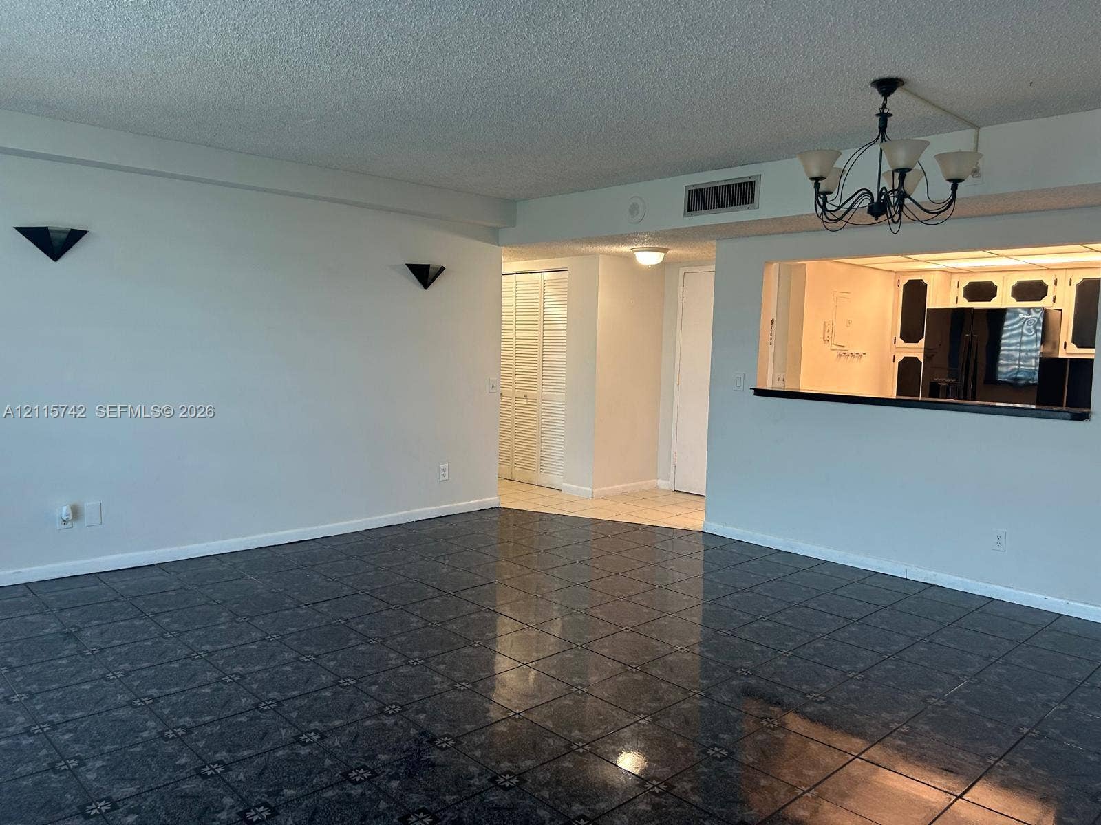 13499 Biscayne Boulevard, #905, North Miami, North Miami, FL 33181 Living area featuring large-format dark floor tile, decorative wall-mounted sconces, a classic chandelier, and an open pass-through window to the kitchen