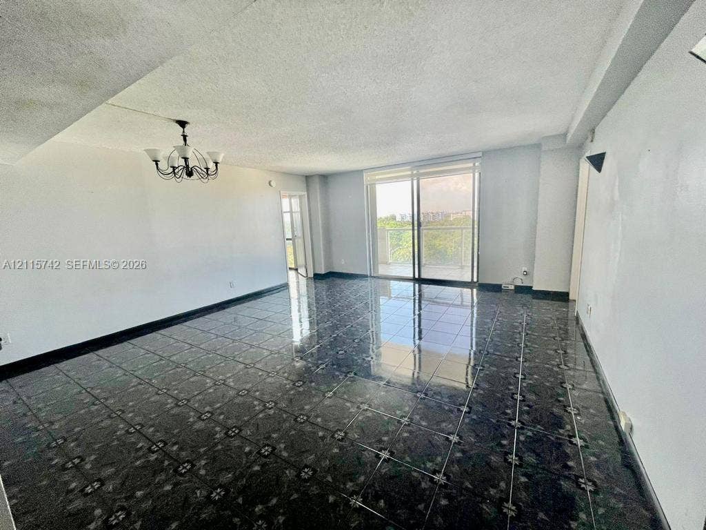 13499 Biscayne Boulevard, #905, North Miami, North Miami, FL 33181 Open-concept living space featuring high-gloss decorative tile flooring, multi-arm metal chandelier, and floor-to-ceiling sliding glass doors opening to a private balcony