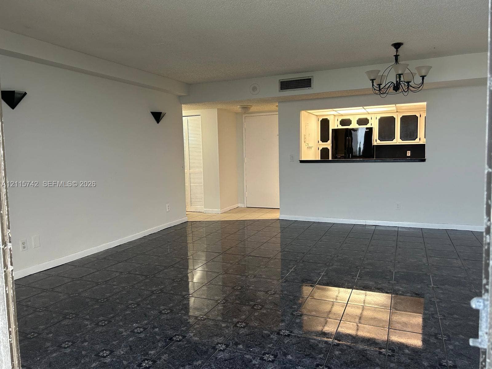 13499 Biscayne Boulevard, #905, North Miami, North Miami, FL 33181 Glossy stone-look tile flooring, pass-through kitchen opening with breakfast bar, traditional multi-arm chandelier, and wall-mounted sconce lighting