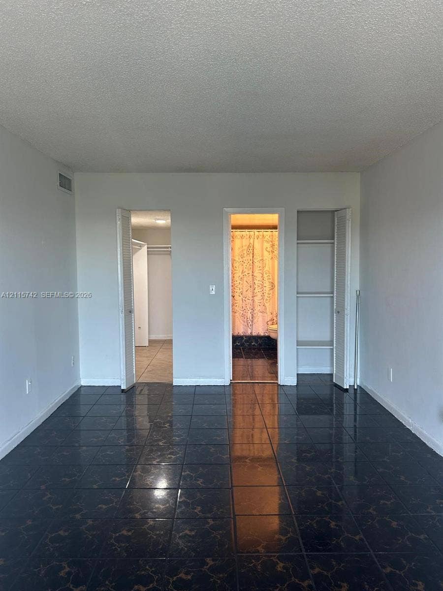 13499 Biscayne Boulevard, #905, North Miami, North Miami, FL 33181 Dark-toned ceramic tile flooring, built-in shelving unit with louvered doors, walk-in closet with hanging rods, and an open doorway featuring a shower area