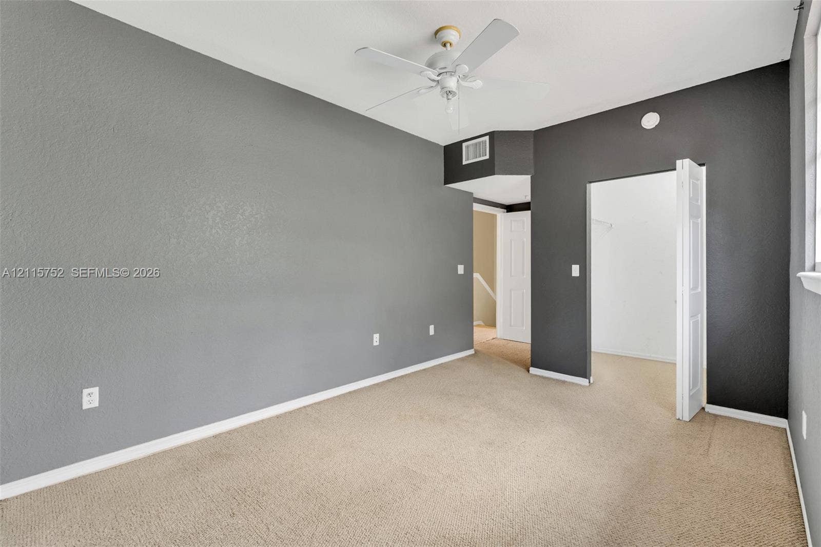 Neutral-toned interior space featuring textured walls, carpeted flooring, a ceiling fan, and a built-in closet with bi-fold doors
