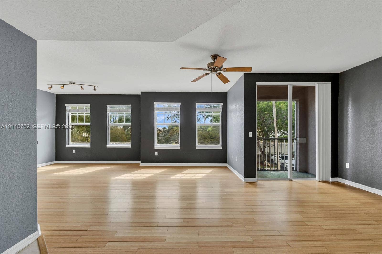 Open-concept interior featuring wood-finish flooring, dark charcoal wall accents, multiple large windows, a ceiling fan, and sliding glass doors