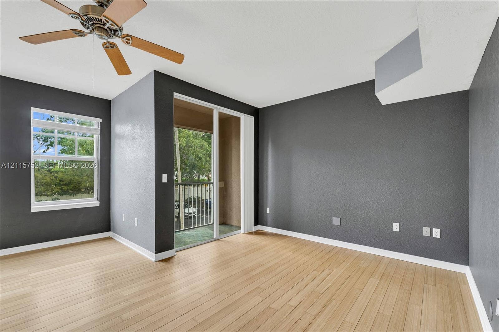 Wood-finish flooring, sliding glass door access to a balcony, ceiling fan with light fixture, and dark-toned walls
