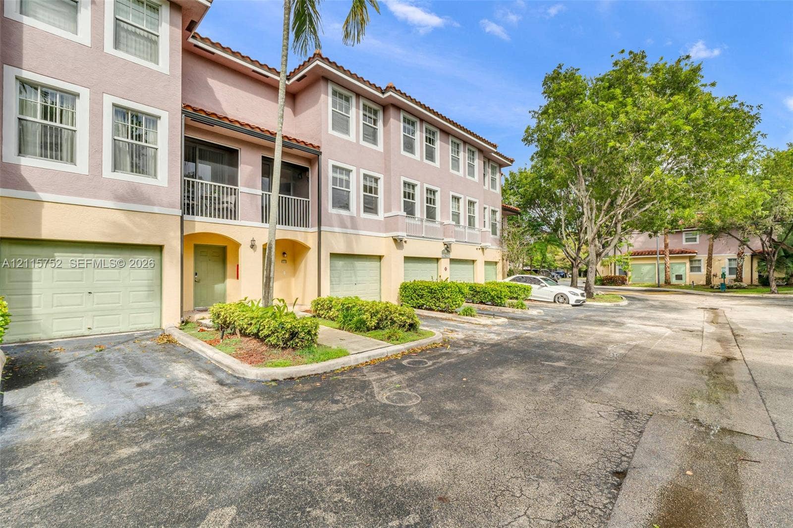 Multi-story exterior featuring a stucco facade, private garage access, second-level balconies, and a tiled roofline