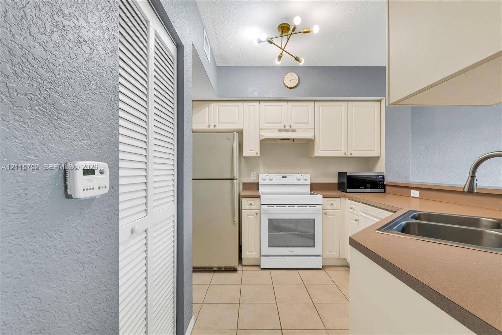 Kitchen featuring off-white cabinetry, solid surface countertops, a dual-basin stainless steel sink, tile flooring, and a multi-bulb geometric ceiling fixture