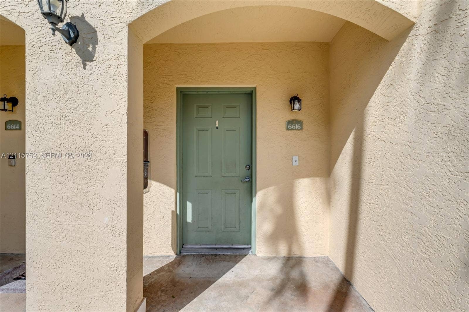 Stucco exterior entry featuring an arched recessed porch, six-panel entry door, and wall-mounted exterior lighting fixtures