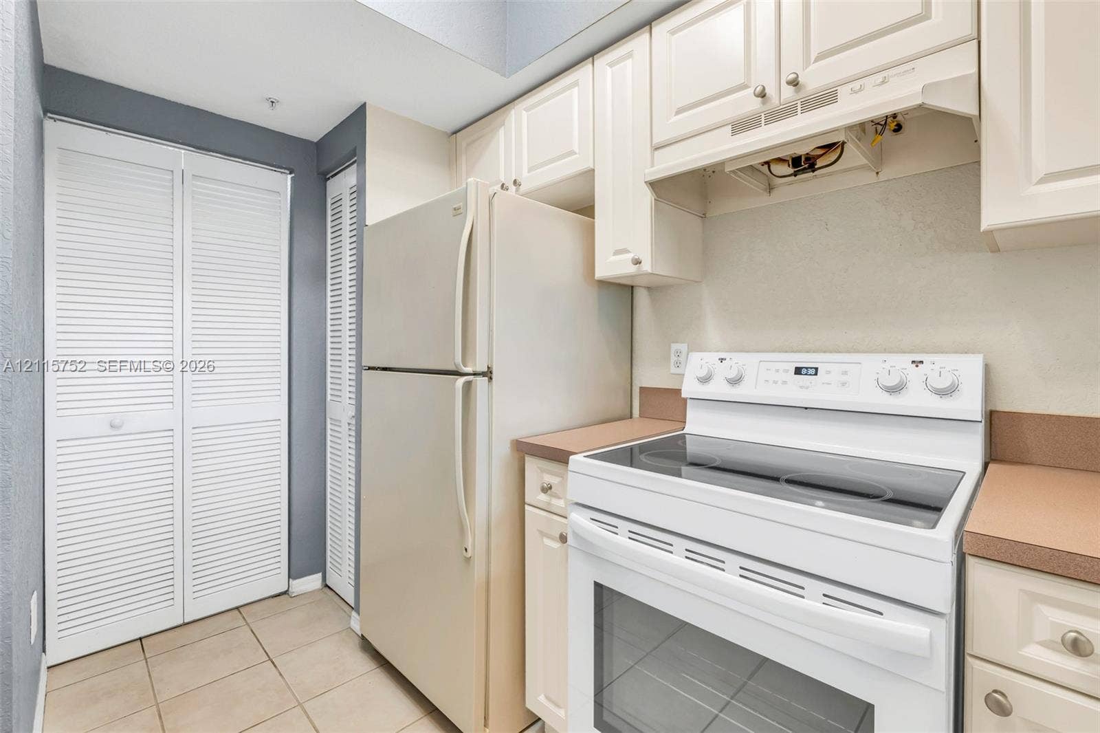Kitchen featuring white louvered cabinetry, solid-surface countertops, tile flooring, and a white electric range