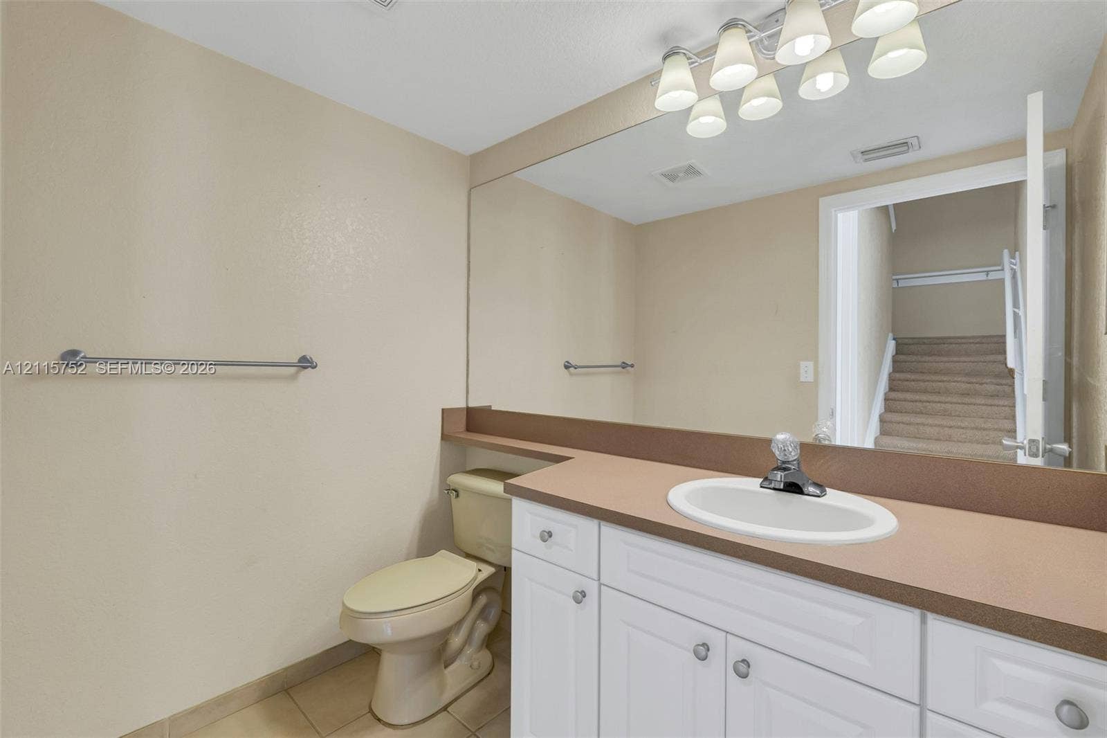 Bathroom featuring a white vanity cabinet with an integrated sink, a large wall-mounted mirror, a multi-bulb light fixture, and a neutral-toned countertop