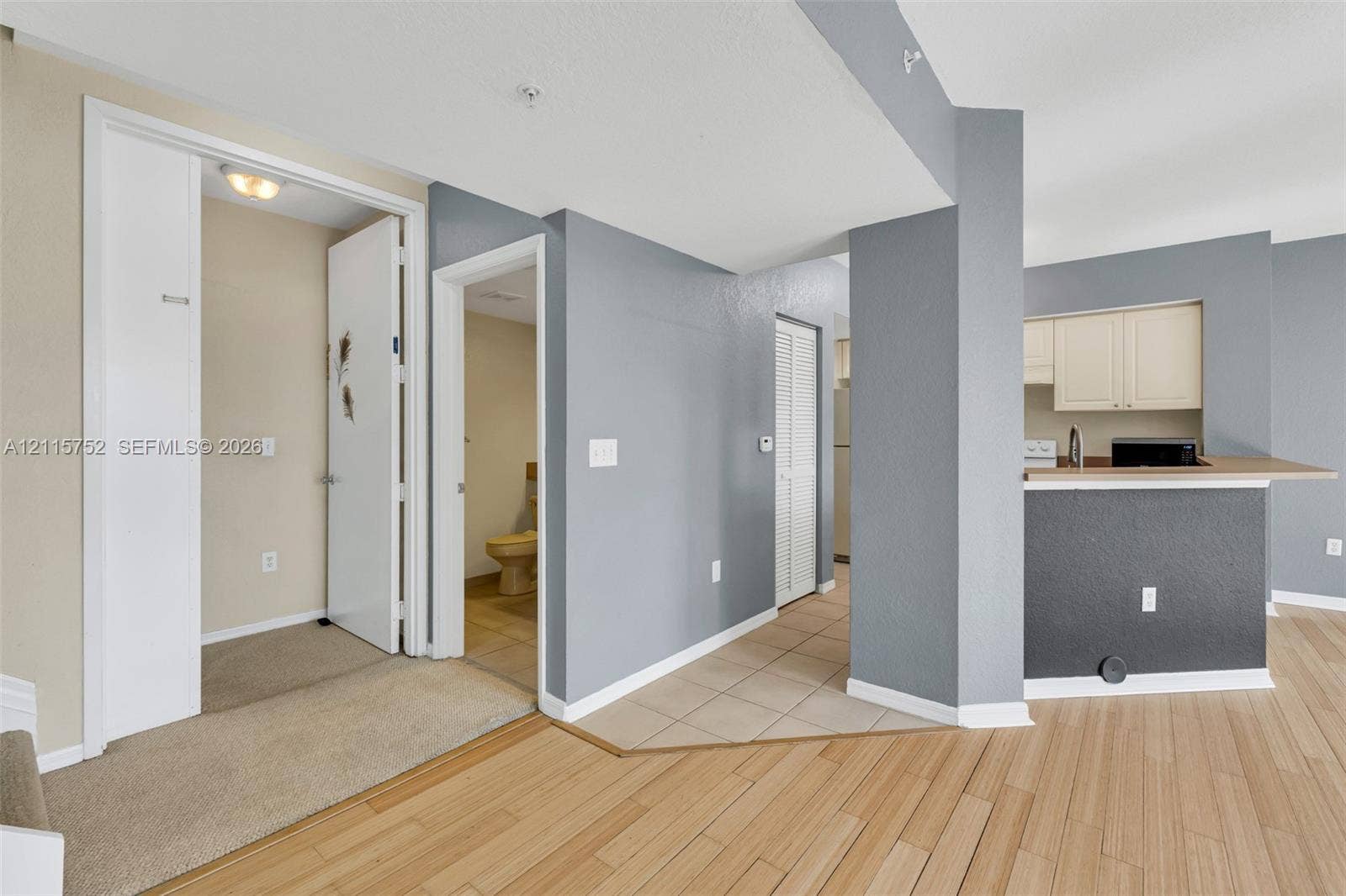 Neutral-toned interior featuring wood-finish flooring, a kitchen breakfast bar with solid-surface countertop, and ceramic tile flooring in the entry