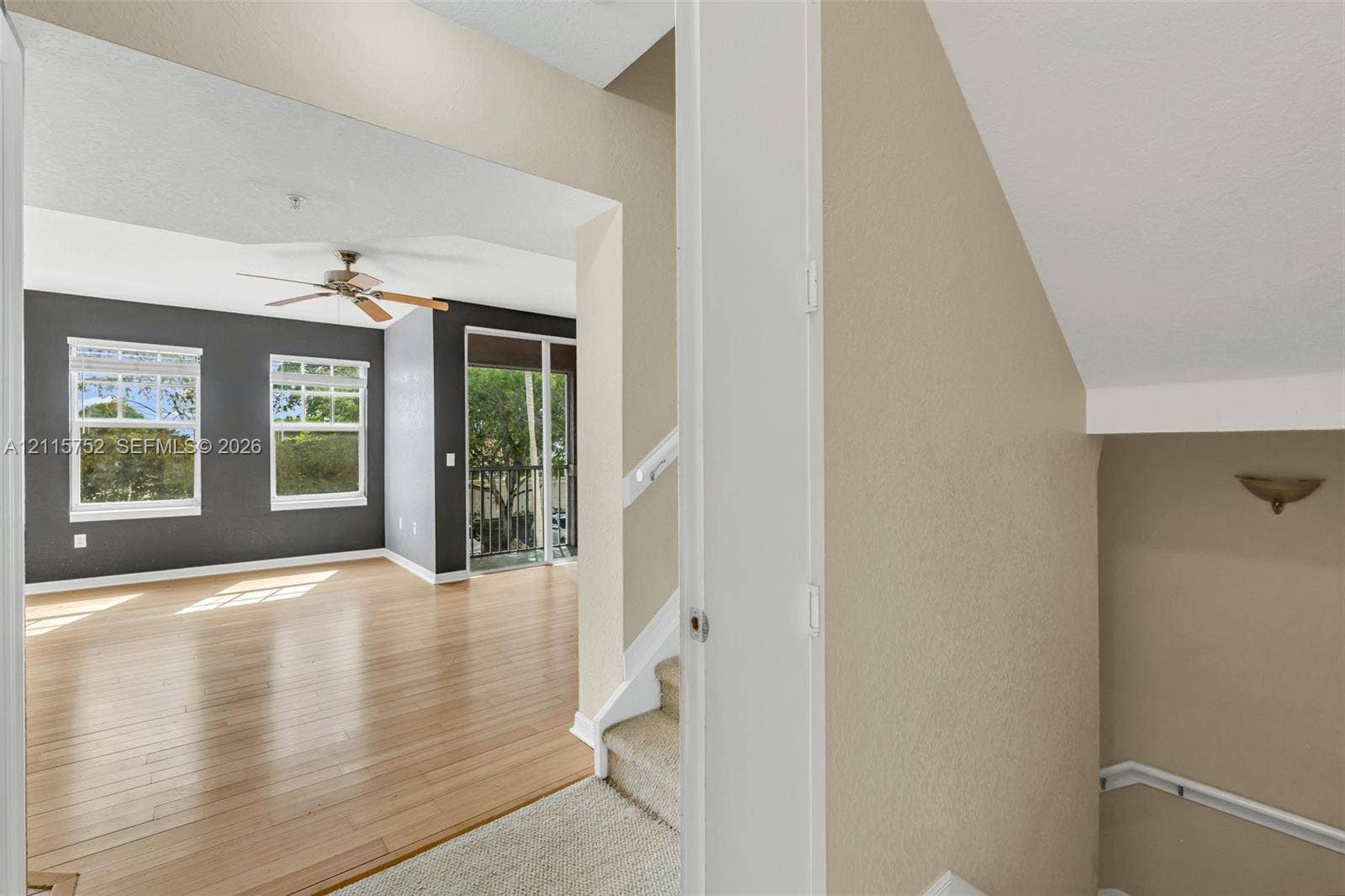 Living area featuring wood-finish flooring, charcoal-toned accent wall, ceiling fan, and large windows with exterior access