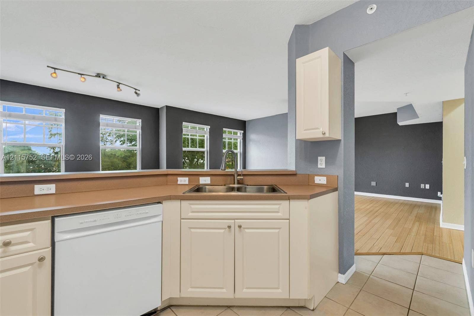 Kitchen area featuring neutral-tone cabinetry, solid-surface countertops, dual-basin undermount sink with a pull-down faucet, tile flooring, and integrated track lighting