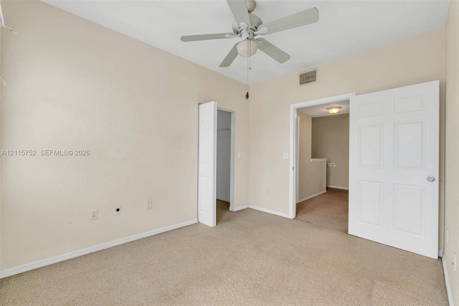 Neutral-toned room featuring carpeting, a white ceiling fan with integrated lighting, and a six-panel door