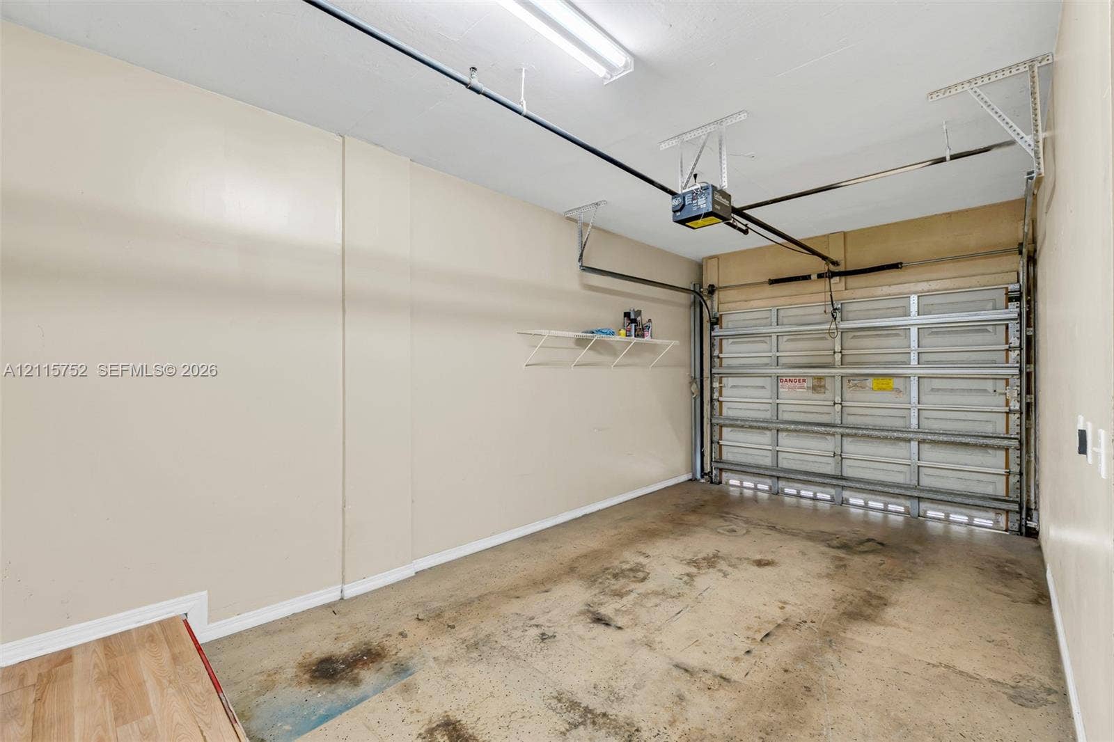 Enclosed garage featuring a sectional metal door, automated door opener, wall-mounted wire shelving, and overhead fluorescent lighting