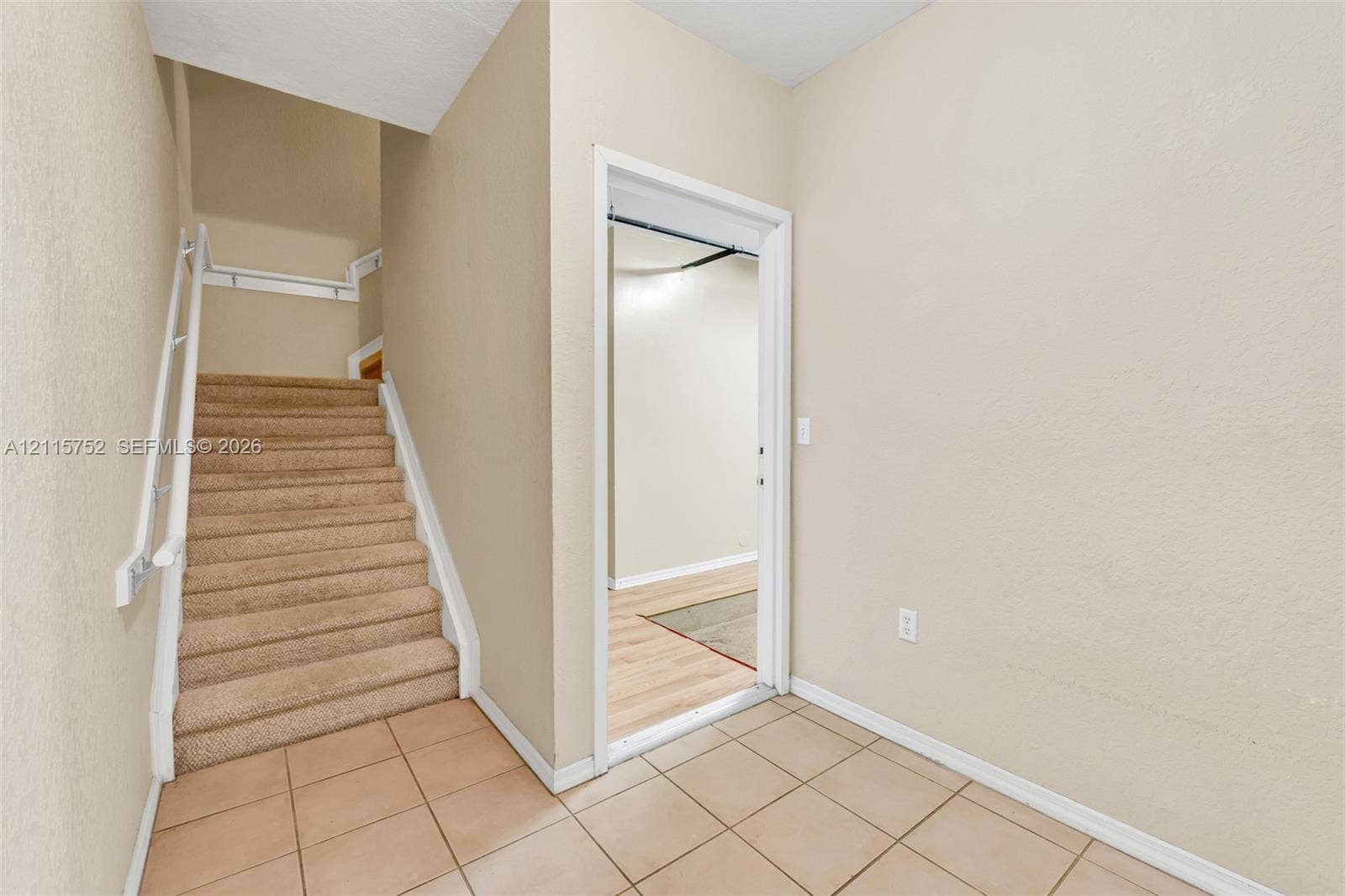 Interior entrance featuring neutral wall tones, carpeted staircase with white handrail, ceramic tile flooring, and interior door frame
