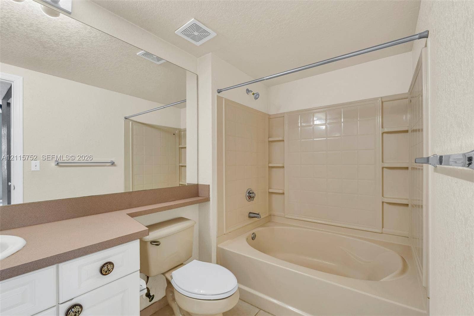 Bathroom featuring a white vanity with a solid-surface countertop, an expansive wall-to-wall mirror, and a molded tub-shower combination with integrated shelving