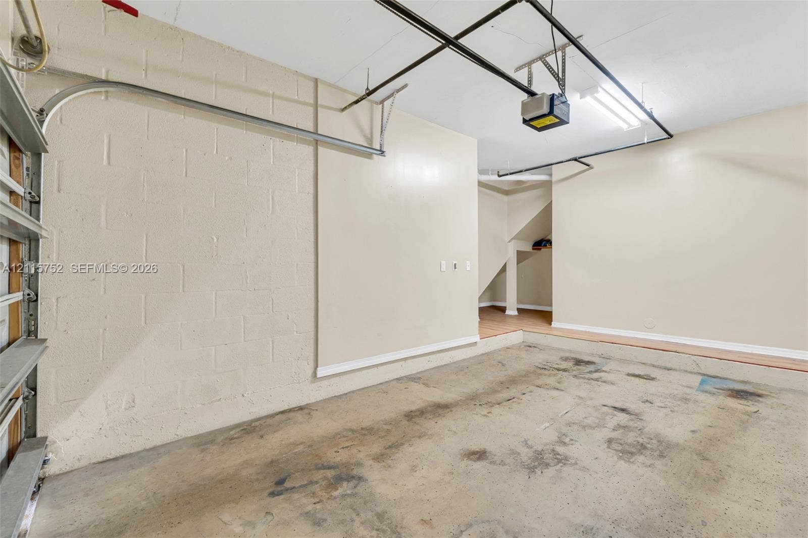Enclosed garage featuring painted concrete block walls, overhead garage door hardware, ceiling-mounted light fixtures, and concrete flooring