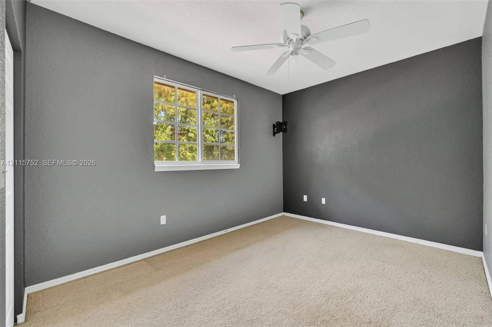 Room featuring charcoal accent walls, neutral wall-to-wall carpeting, a multi-pane window, and a ceiling fan with integrated lighting