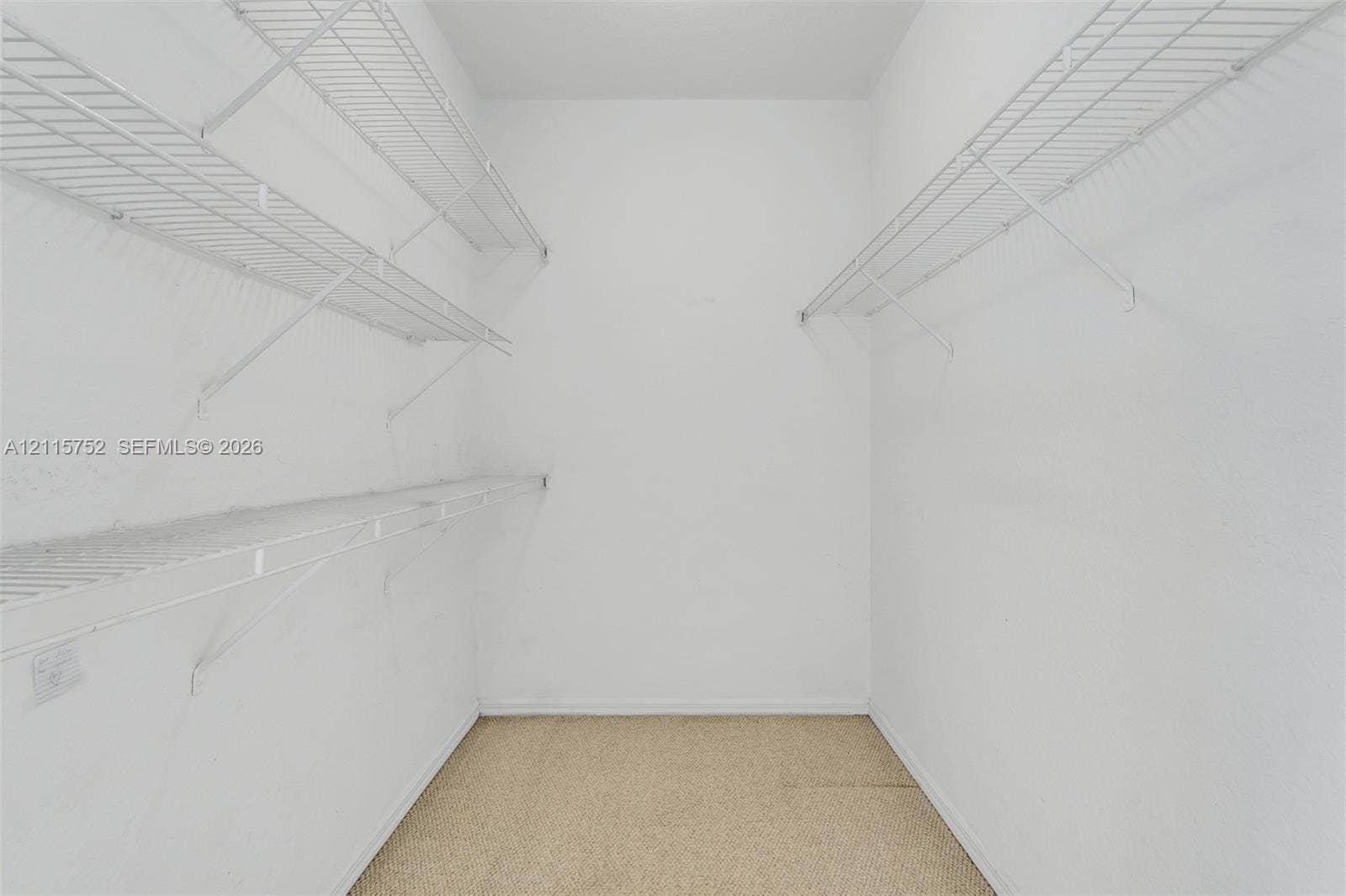 Walk-in storage space featuring neutral carpeting and white, multi-tiered wire shelving units