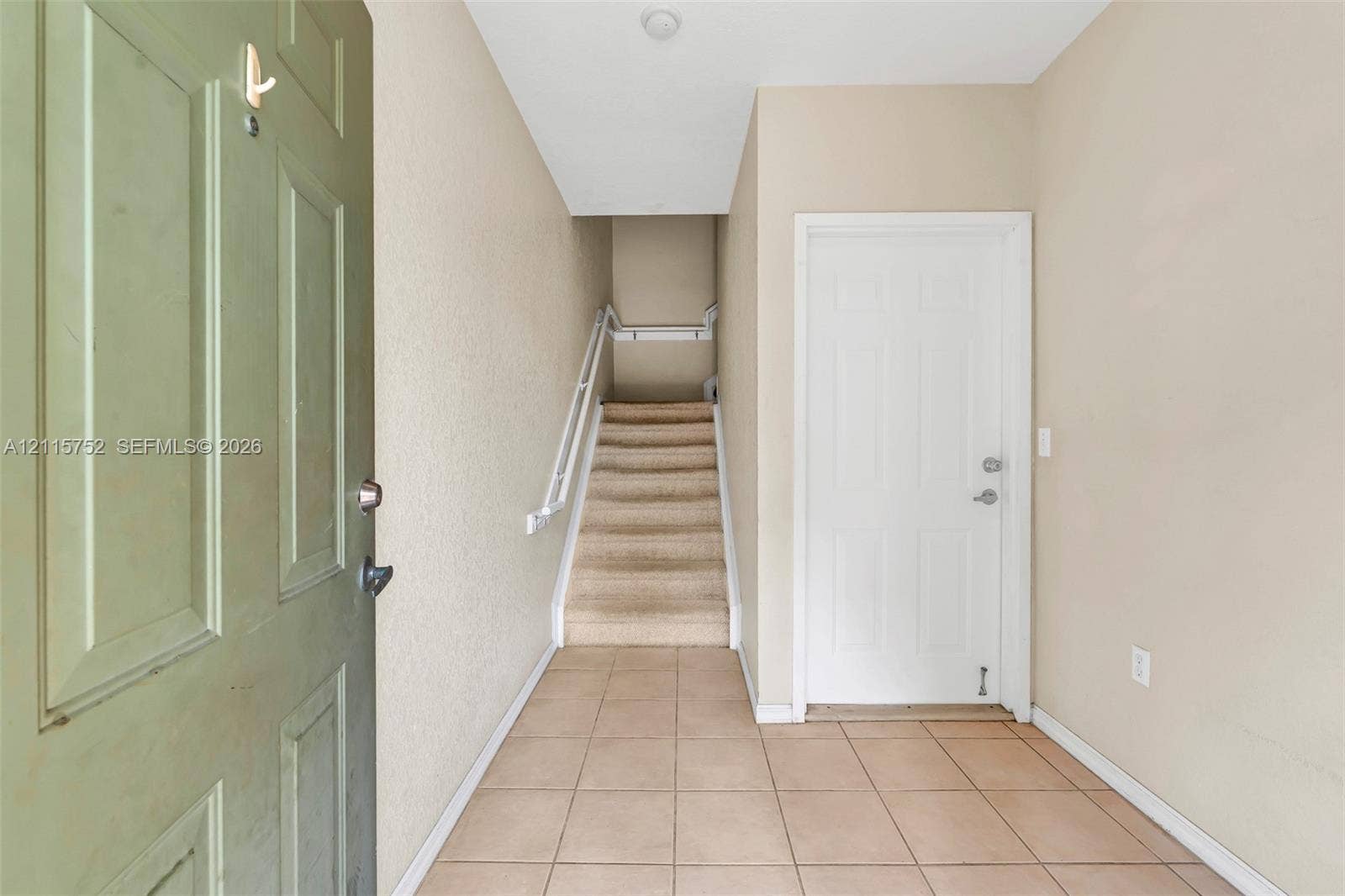 Entryway featuring ceramic tile flooring, a paneled door, and a carpeted staircase with a metal handrail