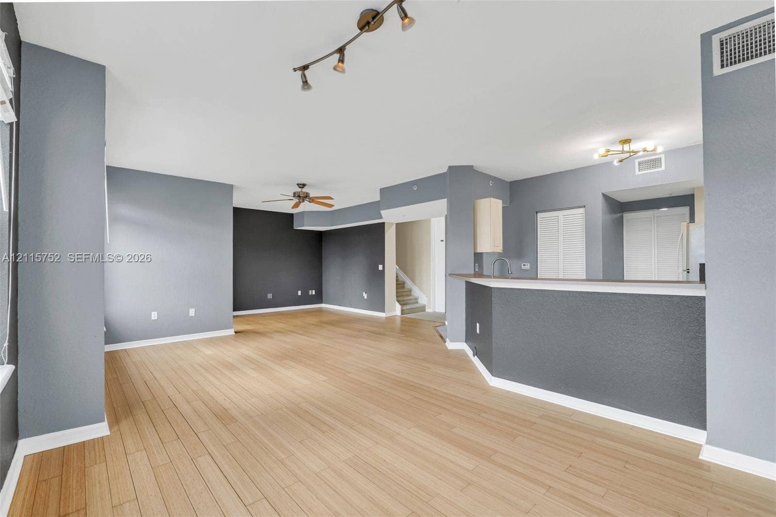 Open-concept interior featuring wood-finish flooring, a tiered breakfast bar with a neutral countertop, track and recessed lighting fixtures, and a ceiling fan