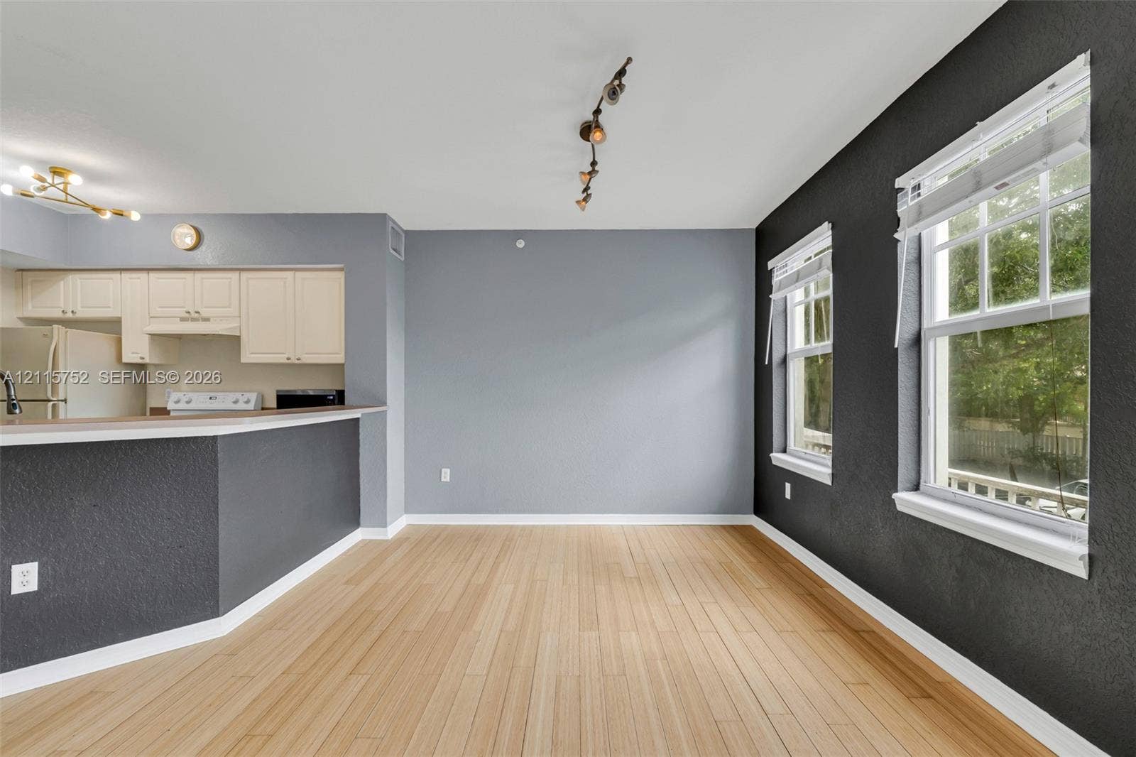 Open-concept interior featuring wood-finish flooring, two-tone wall finishes, a kitchen peninsula with a breakfast bar, and multiple large windows with multi-pane glass