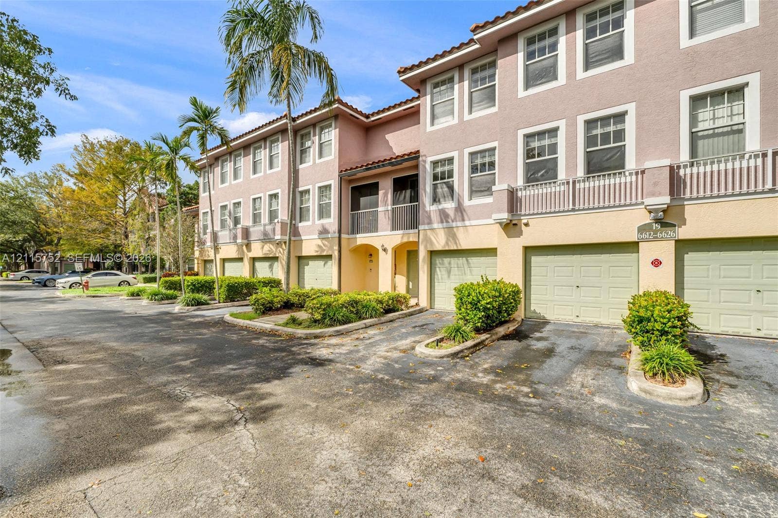 Multi-story stucco exterior featuring tile roofing, individual multi-car garages, private balconies with balustrade railings, and mature palm landscaping