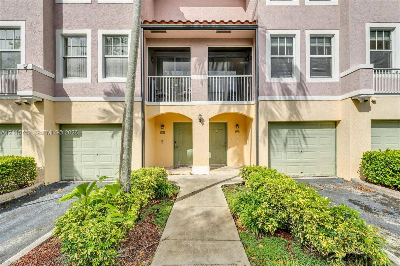 Multi-level exterior featuring a stucco facade, private covered balconies with metal railings, and dual attached garages with sectional doors