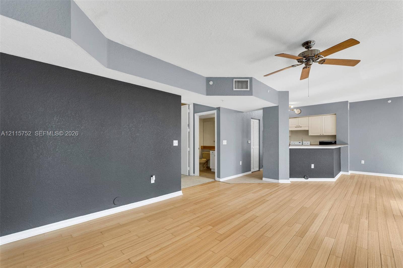 Interior featuring wood-finish flooring, accent wall, tray ceiling, ceiling fan, and kitchen breakfast bar