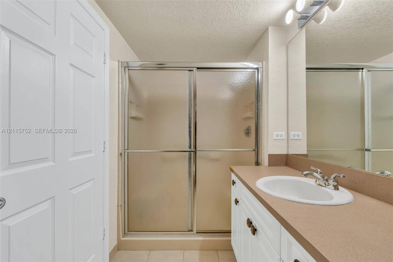 Bathroom featuring a vanity with an integrated basin, chrome faucet, white cabinetry, a glass-enclosed shower, and a full-width mirror