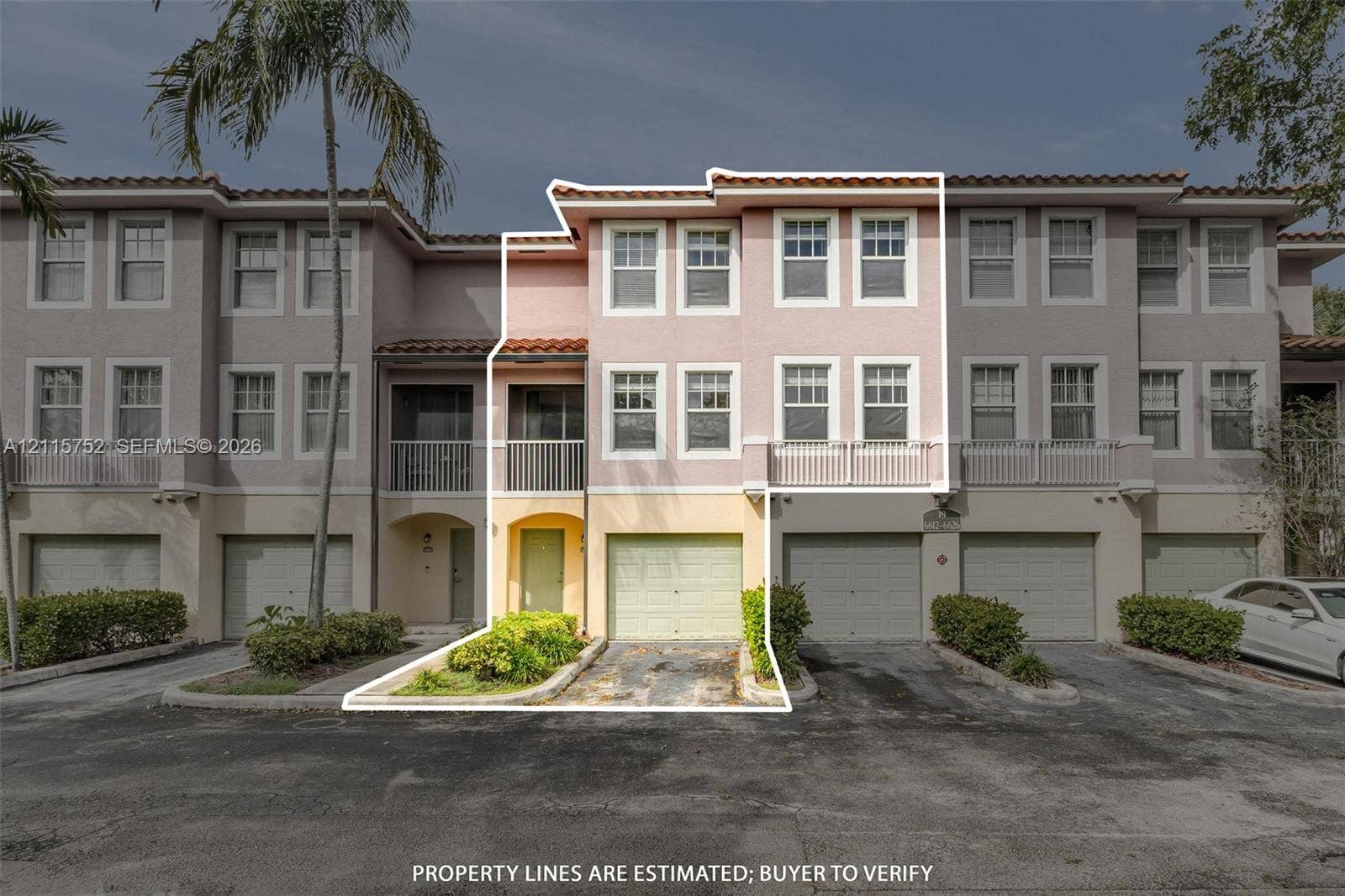 Three-story townhouse exterior featuring a stucco faade, tiled roof, attached garage, and second-level balcony with metal railing