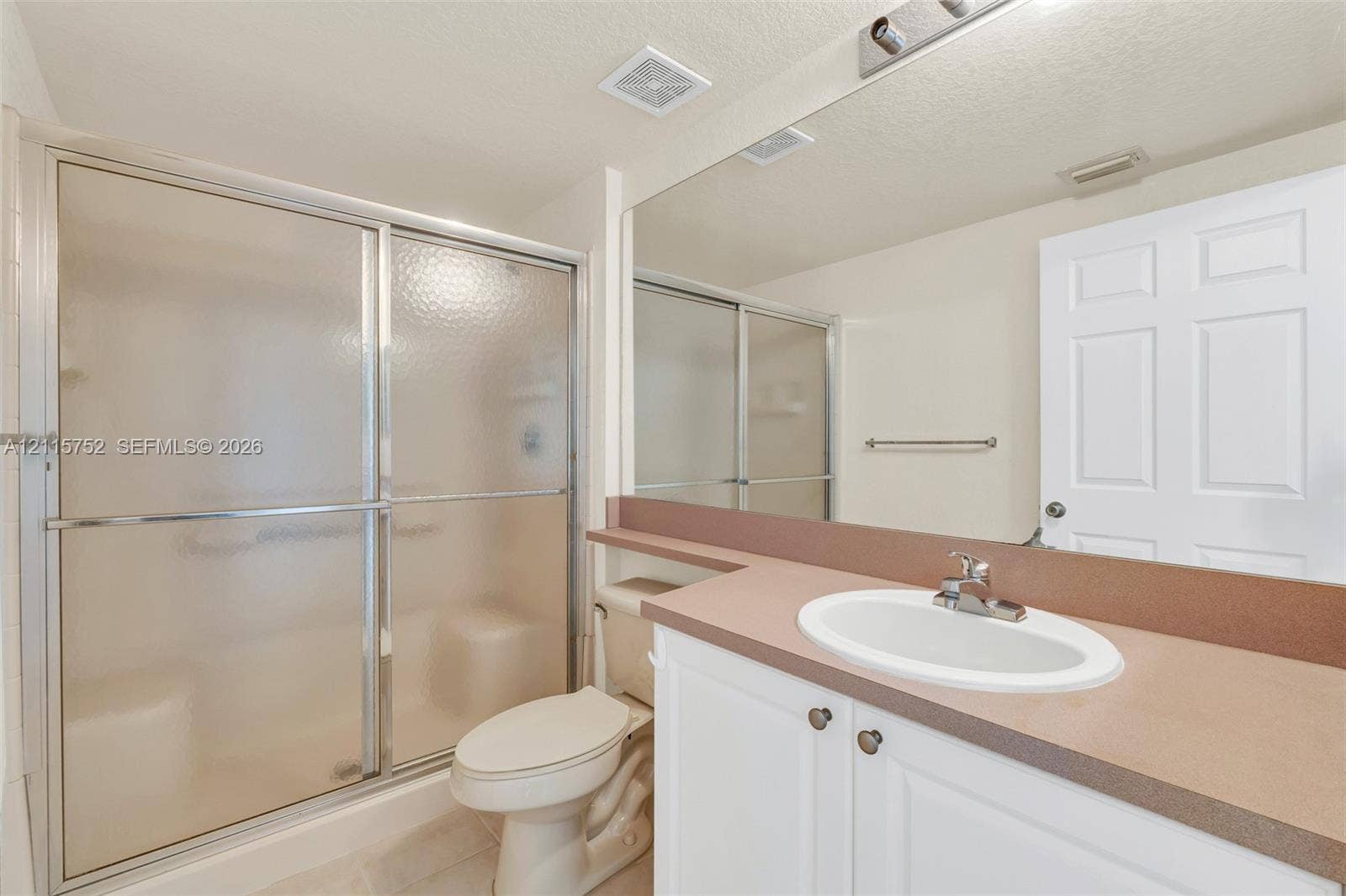 Bathroom featuring a white vanity with a solid-surface countertop, an integrated oval sink, a large wall-mounted mirror, and a walk-in shower with a sliding glass door