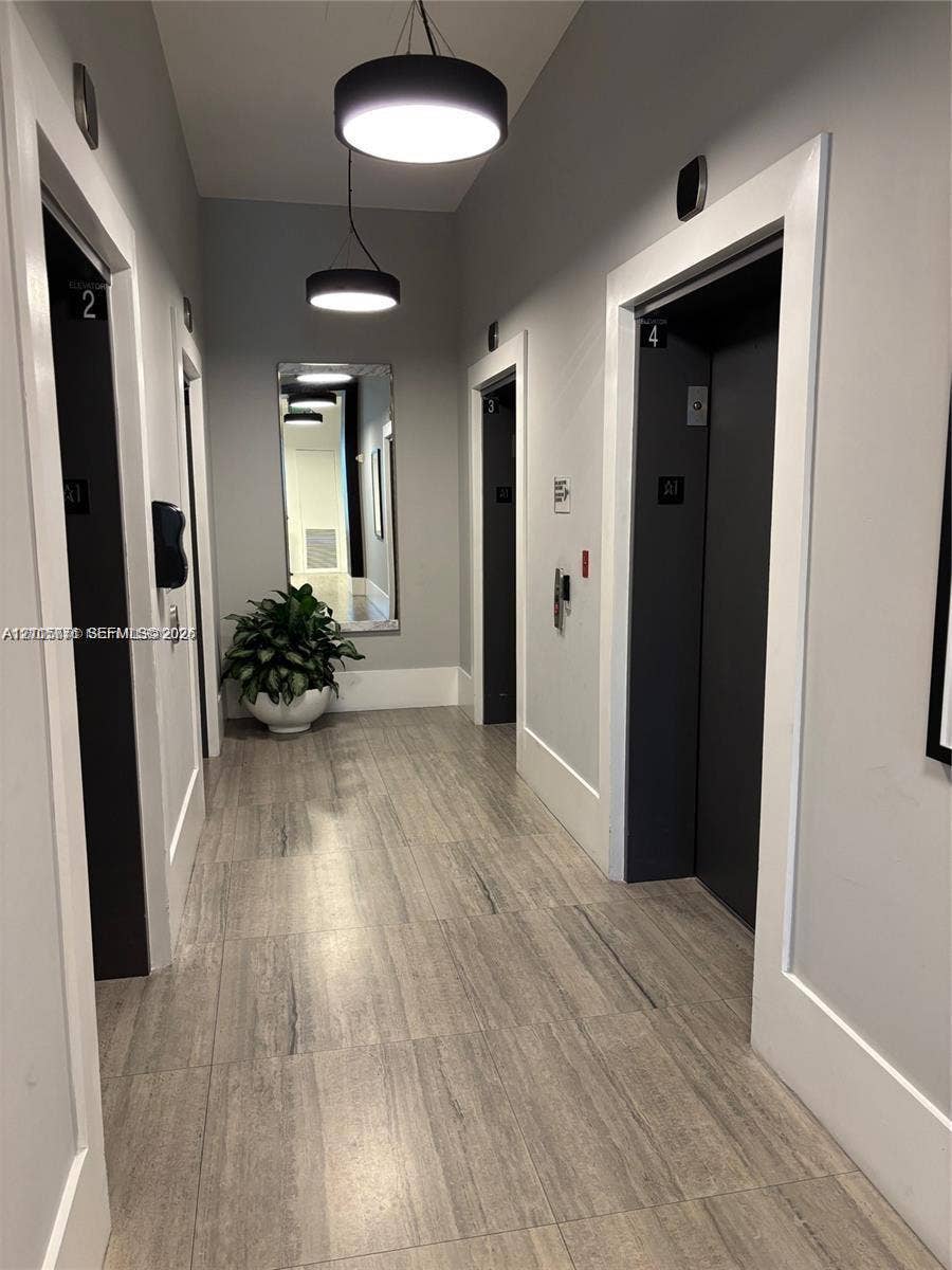 140 S Dixie Highway, #433, Hollywood, Hollywood, FL 33020 Hallway featuring wood-finish tile flooring, matte black elevator doors, wall-mounted modern pendant lighting, and a recessed wall mirror