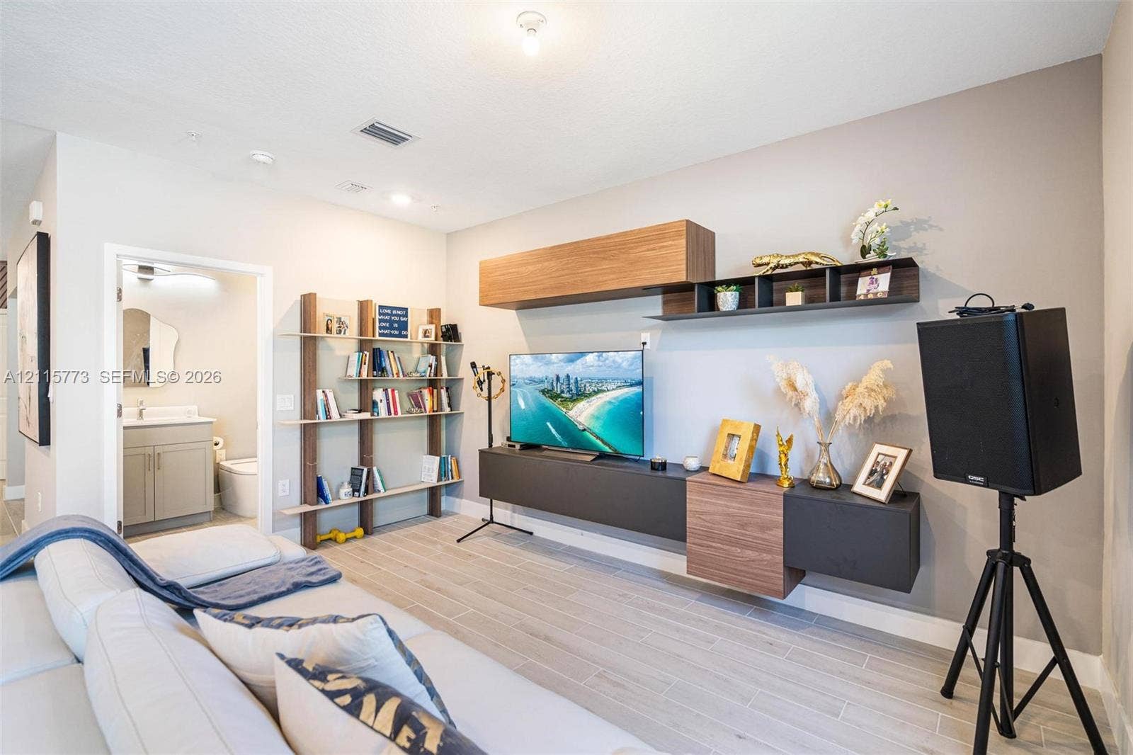 17033 SW 1st Street, #1, Pembroke Pines, Pembroke Pines, FL 33027 Living area featuring wood-finish flooring, a wall-mounted multi-piece media console with wood and matte-finish cabinetry, and a tiered built-in shelving unit