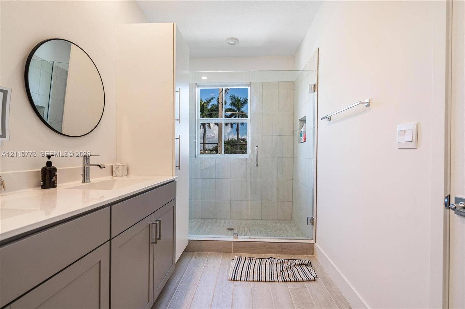 17033 SW 1st Street, #1, Pembroke Pines, Pembroke Pines, FL 33027 Bathroom featuring a neutral-toned vanity with a solid-surface countertop, glass-enclosed walk-in shower with tiled surround, wood-finish flooring, and a circular wall-mounted mirror