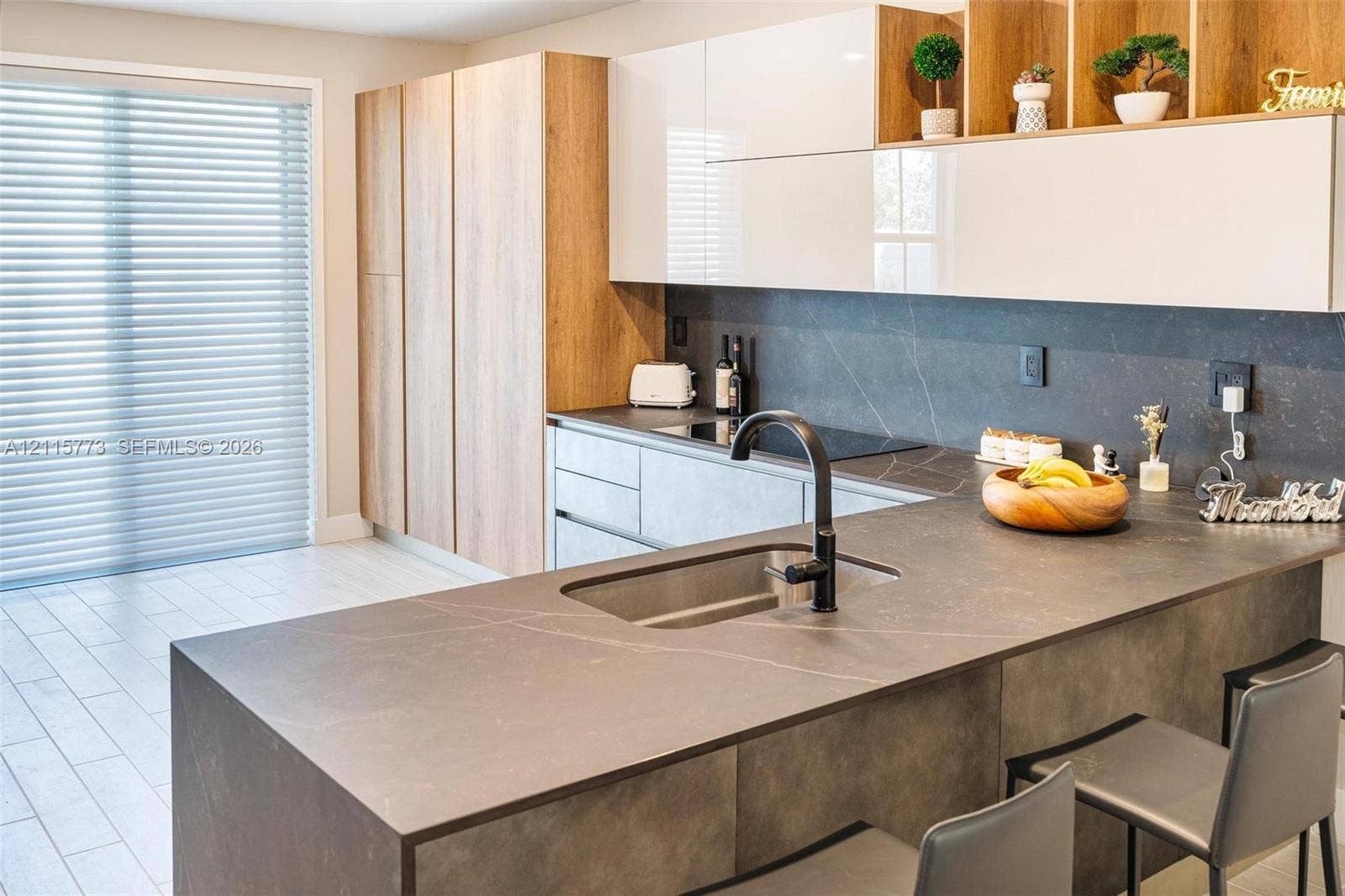 17033 SW 1st Street, #1, Pembroke Pines, Pembroke Pines, FL 33027 Kitchen featuring two-tone cabinetry with wood-finish vertical panels and white upper cabinets, expansive dark stone-finish countertops, undermount stainless steel sink, matte black gooseneck faucet, and light-toned tile flooring
