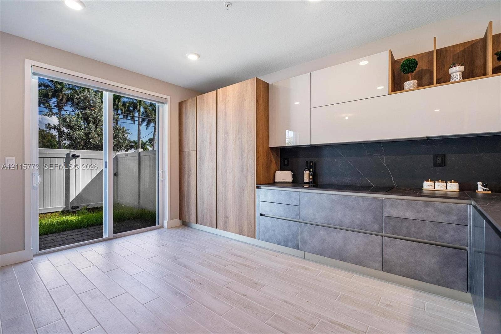 17033 SW 1st Street, #1, Pembroke Pines, Pembroke Pines, FL 33027 Contemporary kitchen featuring flat-panel cabinetry in wood-finish and high-gloss white, dark stone-finish countertops, integrated cooktop, and large-format tile flooring with a sliding glass door providing exterior access