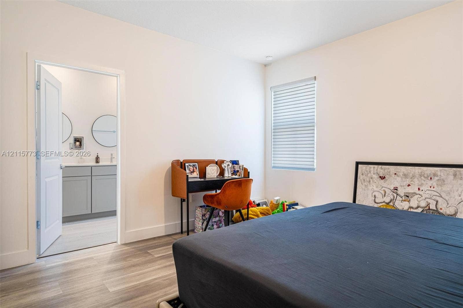 17033 SW 1st Street, #1, Pembroke Pines, Pembroke Pines, FL 33027 Neutral-toned room featuring wood-finish flooring, horizontal window blinds, and an interior door opening to a bathroom with a gray dual-sink vanity