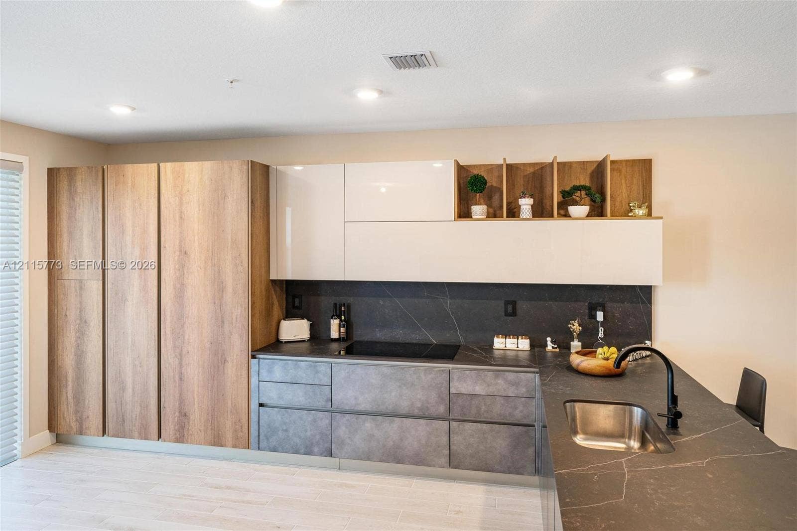 17033 SW 1st Street, #1, Pembroke Pines, Pembroke Pines, FL 33027 Kitchen featuring high-gloss white upper cabinetry, integrated wood-finish full-height storage, matte stone-texture lower cabinetry, stone-finish countertops, and an undermount stainless steel sink with a matte black faucet