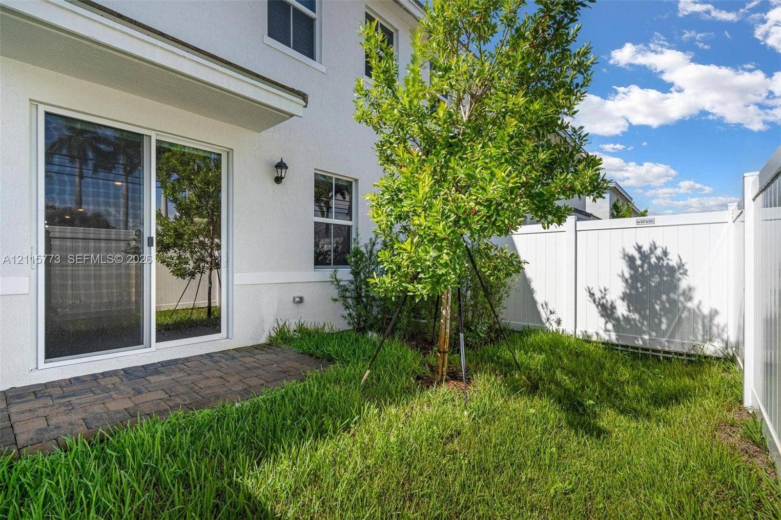 17033 SW 1st Street, #1, Pembroke Pines, Pembroke Pines, FL 33027 Paver patio, grass yard, white vinyl privacy fencing, and exterior wall-mounted lighting
