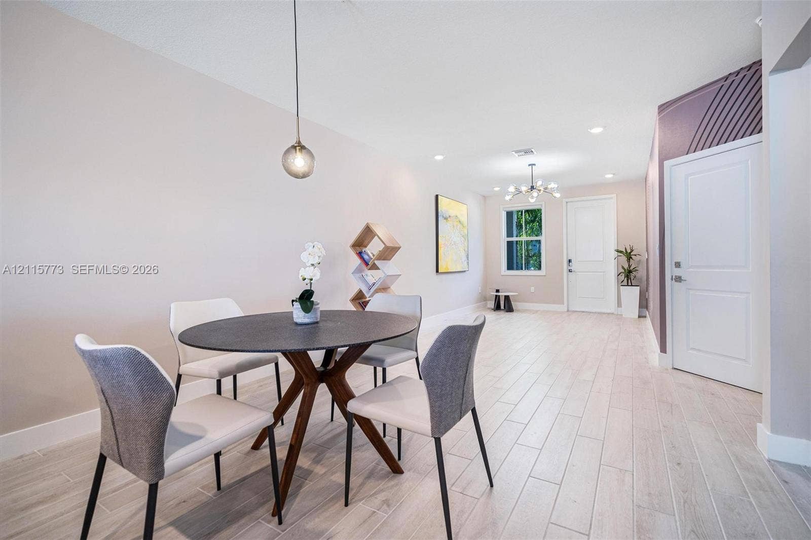17033 SW 1st Street, #1, Pembroke Pines, Pembroke Pines, FL 33027 Open-concept area featuring light-toned wood-finish flooring, a contemporary globe pendant light, an multi-arm chandelier, and an accent wall with geometric detail