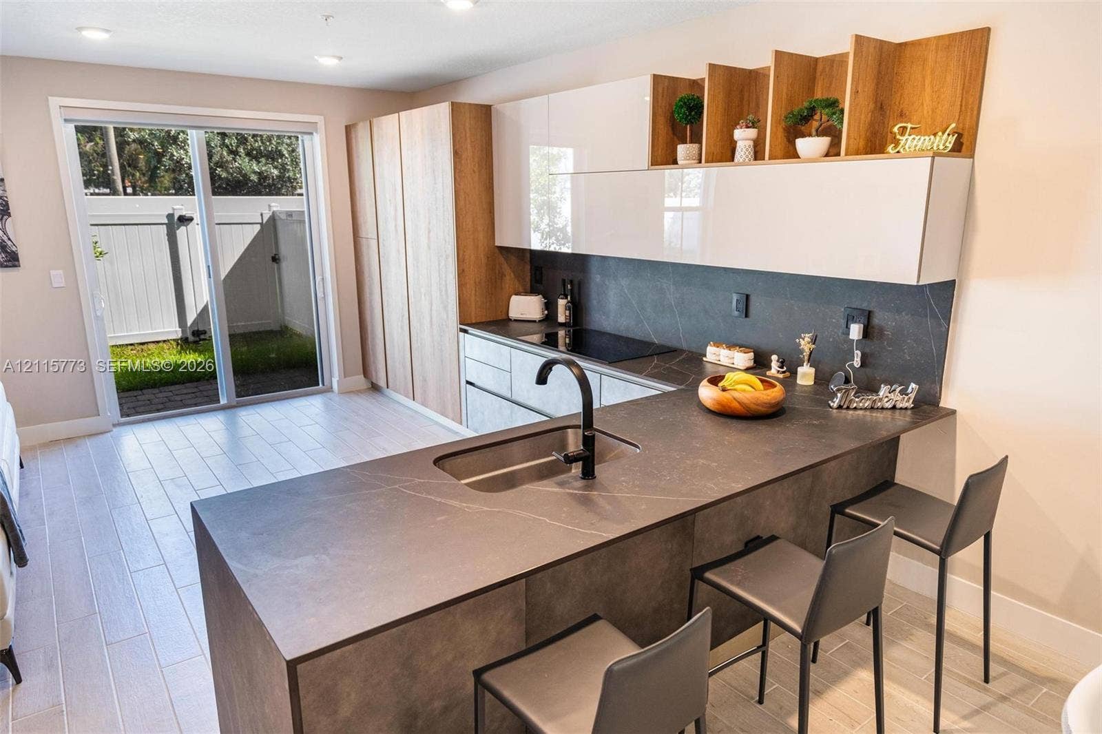 17033 SW 1st Street, #1, Pembroke Pines, Pembroke Pines, FL 33027 Kitchen featuring two-tone cabinetry with wood-finish accents, matte-finish countertops with integrated sink, dark faucet, built-in cooktop, and glass sliding doors leading to a patio area