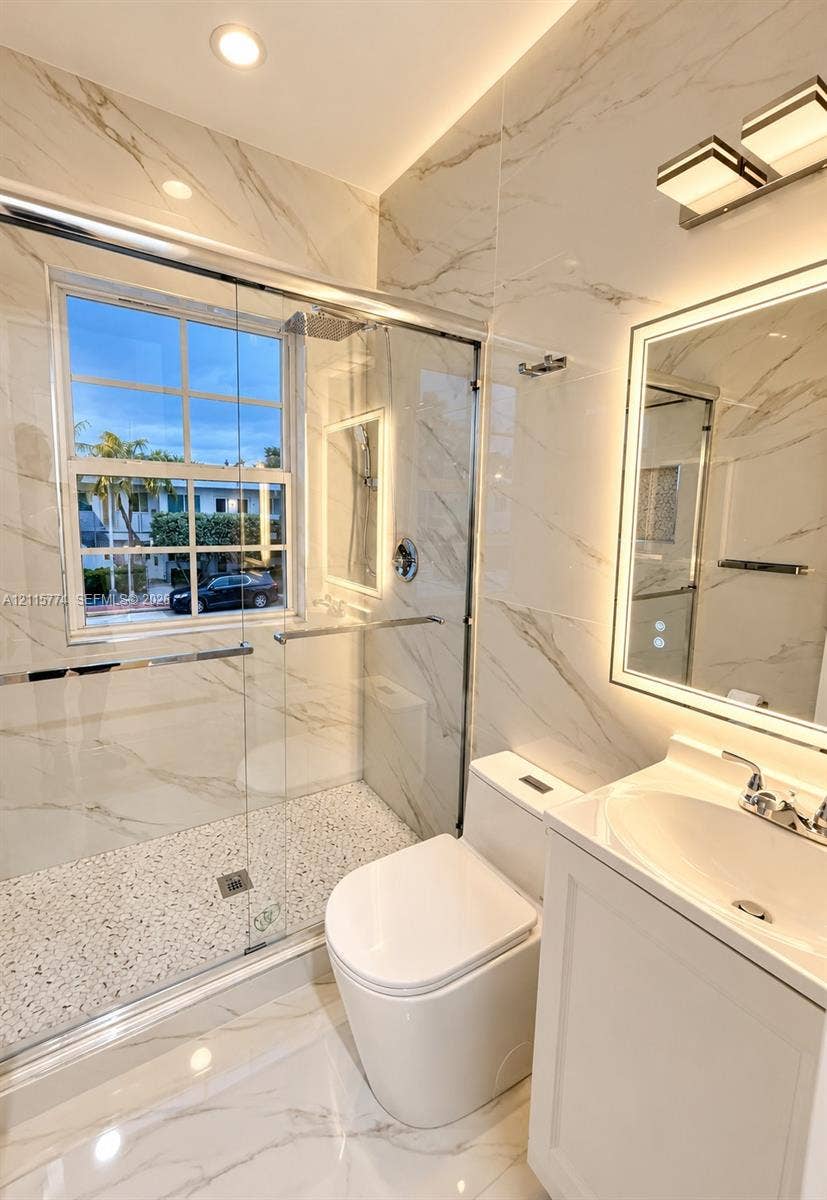 1455 Michigan Avenue, #19A, Miami Beach, Miami Beach, FL 33139 Full-height stone-look wall tile, walk-in shower with pebble-finish flooring and frameless glass enclosure, backlit LED vanity mirror, white cabinetry with integrated sink, and recessed lighting