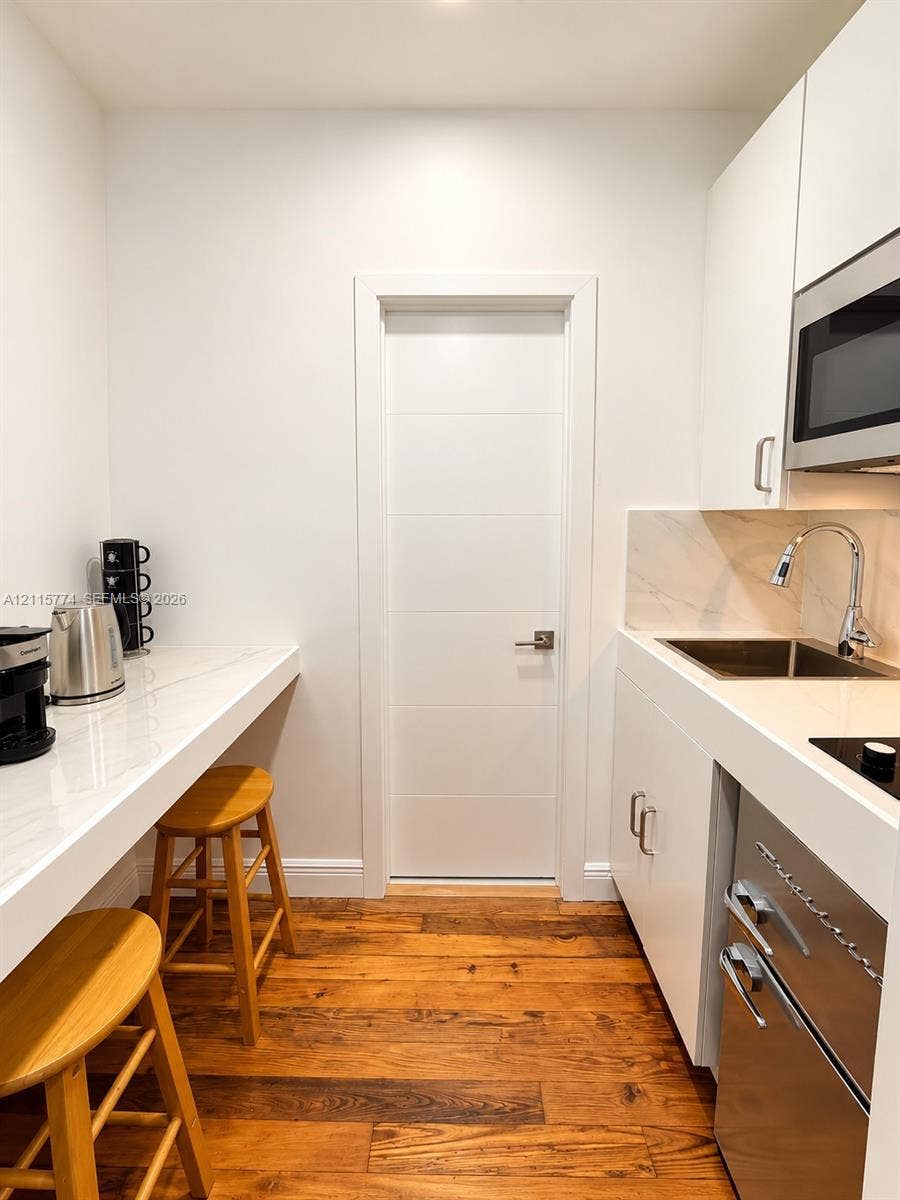 1455 Michigan Avenue, #19A, Miami Beach, Miami Beach, FL 33139 Kitchenette featuring white flat-panel cabinetry, stone-finish countertops, stainless steel undermount sink with arched faucet, built-in microwave, and wood-finish flooring